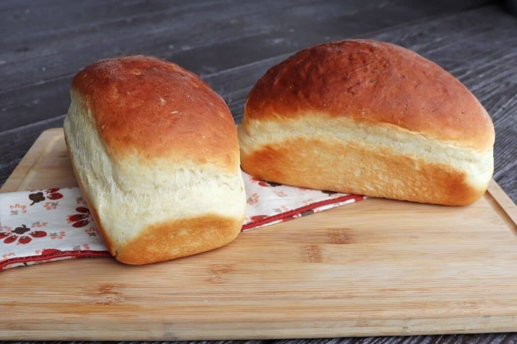 Two loaves of mashed potato bread sitting on a napkin on a wooden cutting board.