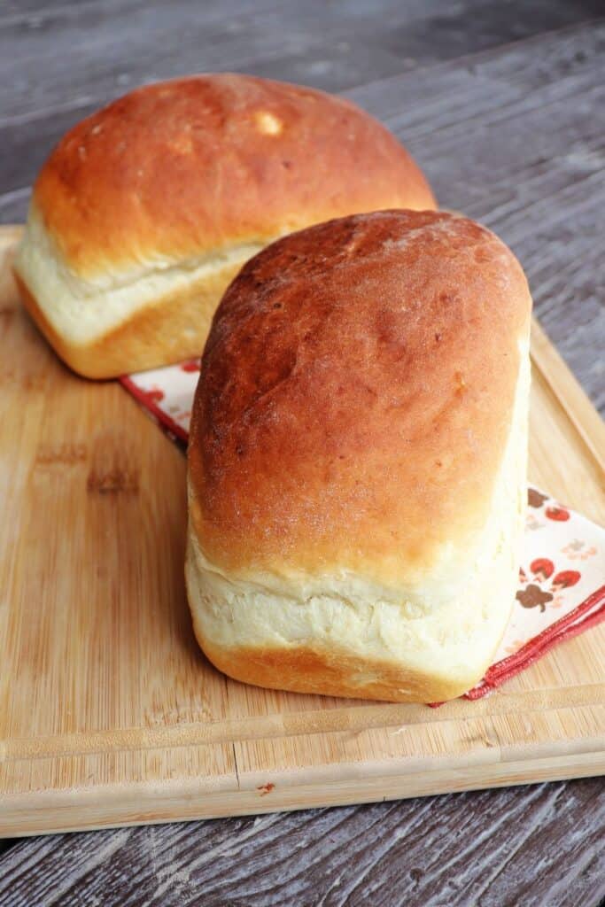 Two loaves of mashed potato bread sitting on top of a napkin on a wooden cutting board.