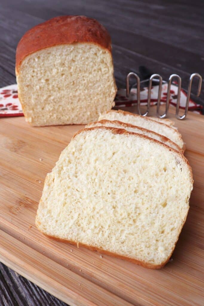 Slices of mashed potato bread on a board with remaining loaf and metal potato masher in the background.