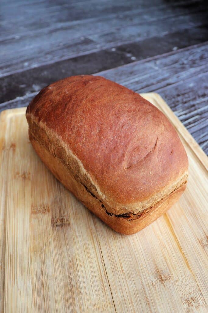 A loaf of brown molasses bread sitting on a wooden cutting board as seen from above.