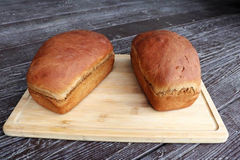 2 loaves of brown molasses bread sitting on a wooden cutting board.
