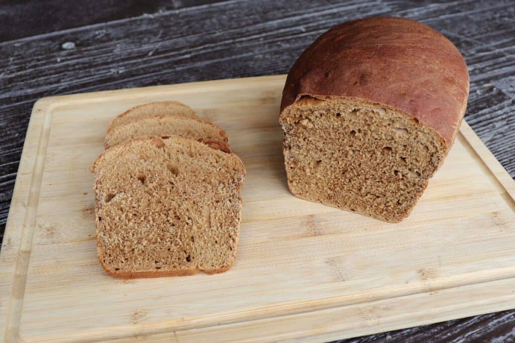 Slices of molasses bread sitting on a wooden board next to the remaining whole loaf.