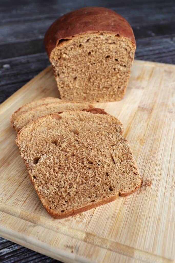 Slices of molasses bread on a wooden cutting board with remaining loaf sitting behind them.