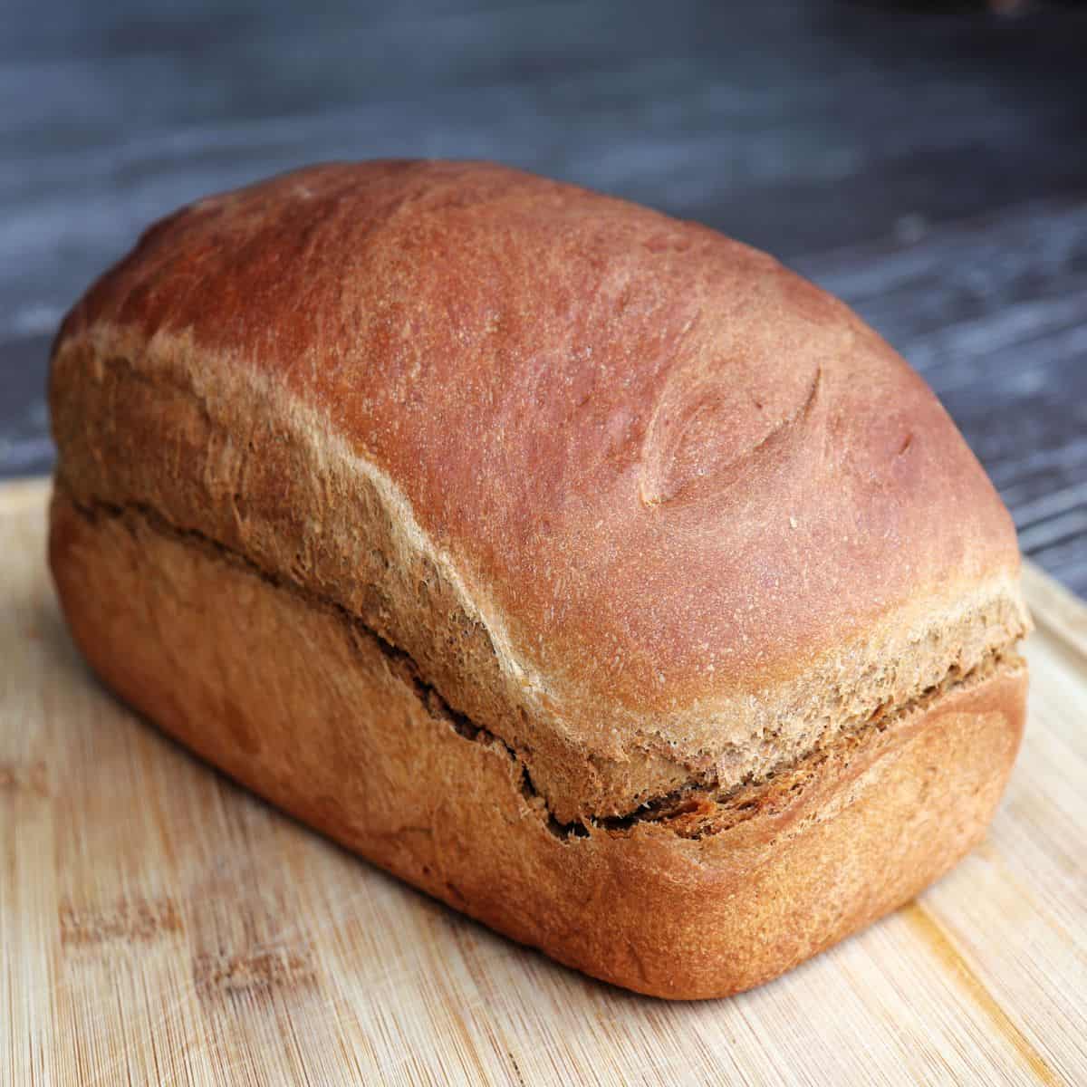 A loaf of brown molasses bread on a wooden cutting board.