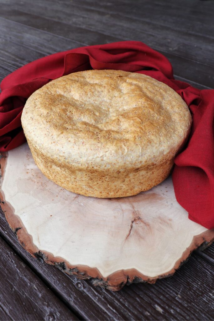 A loaf of shepherd's bread sitting on a board surrounded by a red cloth.