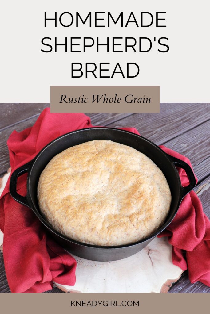 A loaf of bread sitting in a black, round Dutch oven on a board surrounded by a red cloth. Text overlay reads: Homemade Shepherd's Bread Rustic Whole Grain.