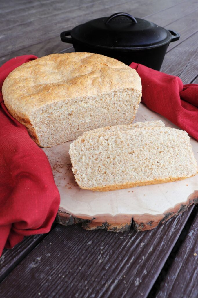 Slices of shepherd's bread sitting on a cutting board with remaining loaf behind them. A red cloth surrounds the bread and black Dutch oven sits in the background.