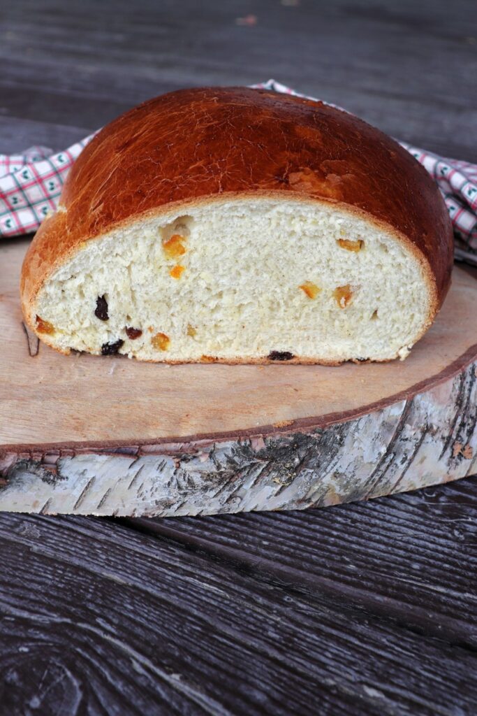 A loaf of julekake with the end cut off exposing the insides studded with bits of dried fruits sitting on a wooden board.