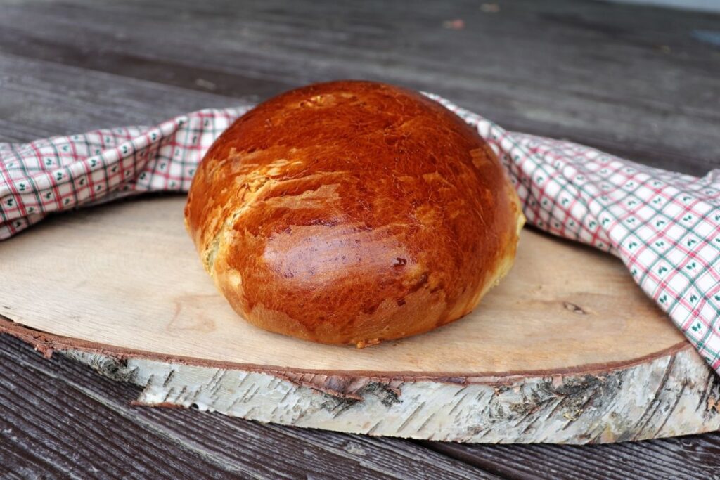 A round loaf of bread sitting on a slice of log surrounded by a cloth.