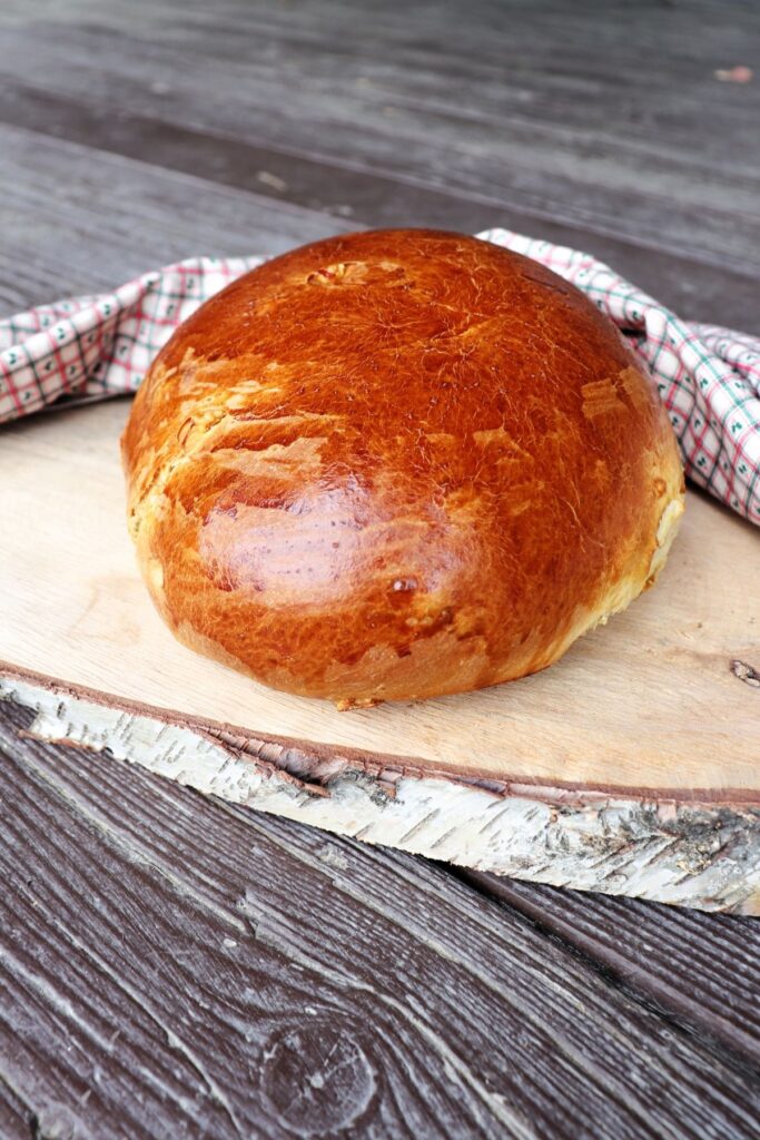 A round loaf of bread sitting on a slice of log surrounded by a cloth.