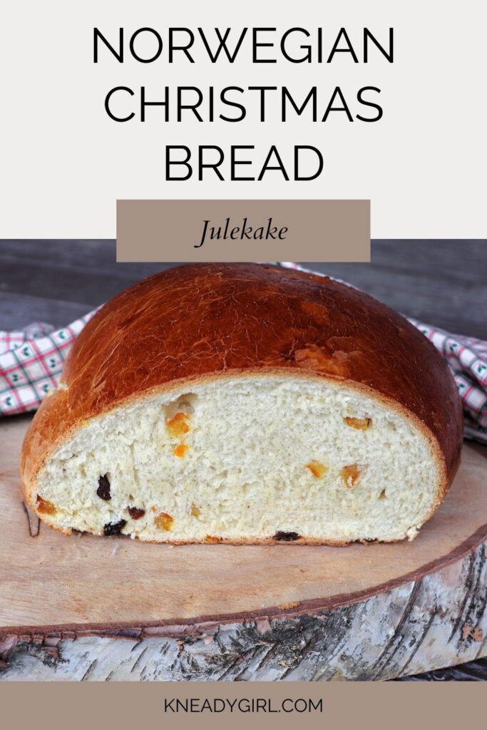 A loaf of julekake with the end cut off exposing the insides studded with bits of dried fruits sitting on a wooden board. A text overlay reads: Norwegian Christmas Bread - Julekake.