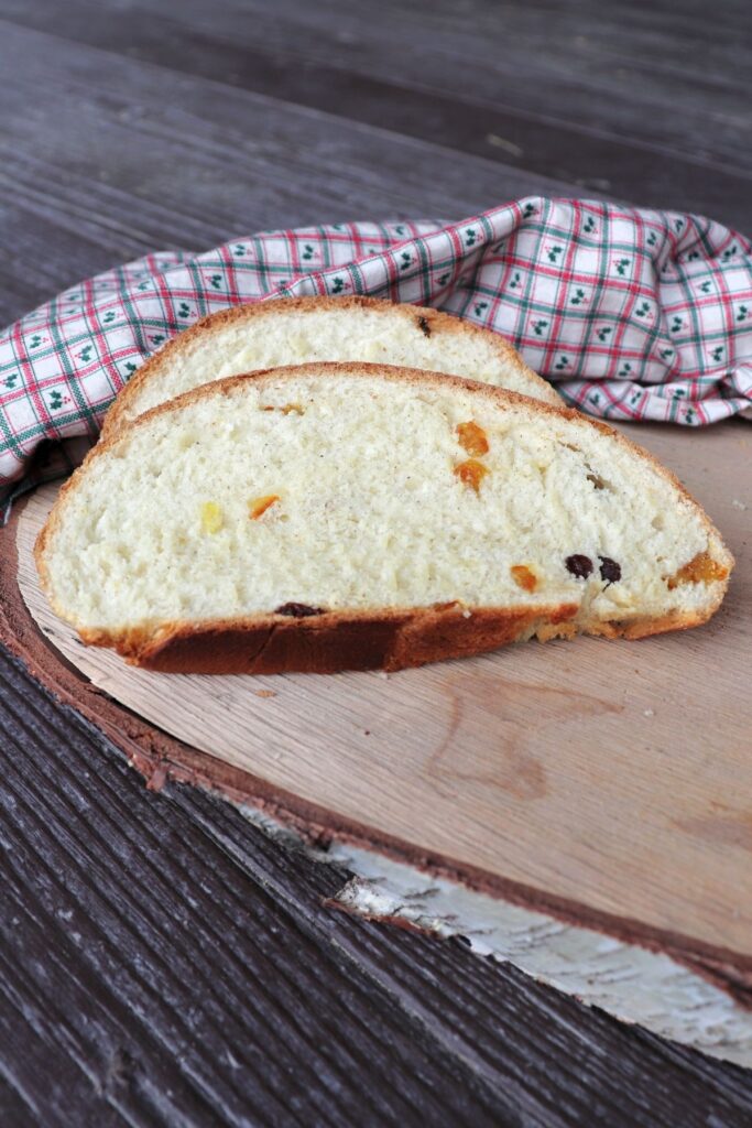 Slices of julekake sitting on a board with a cloth behind them.