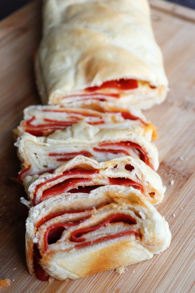 Slices of bread exposing layers of bread, cheese and pepperoni on a board.