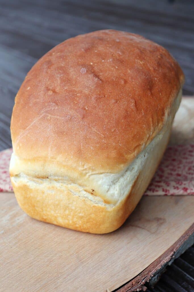 A loaf of white bread sitting on a board with a pink cloth.