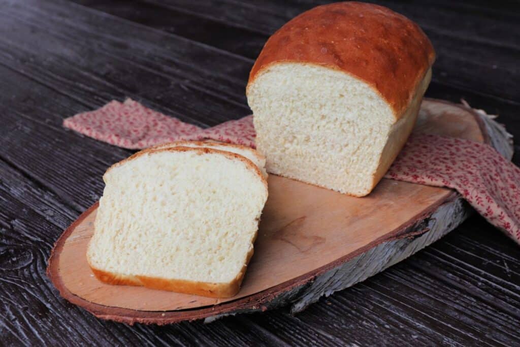 Slices of white bread sitting on a board with the remaining loaf sitting on a pink cloth behind them.