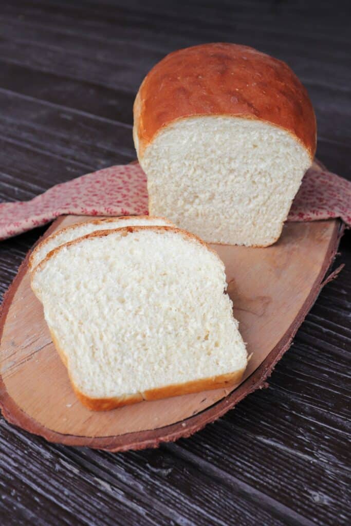 Slices of white bread sitting on a board with the remaining loaf sitting on a pink cloth behind them.