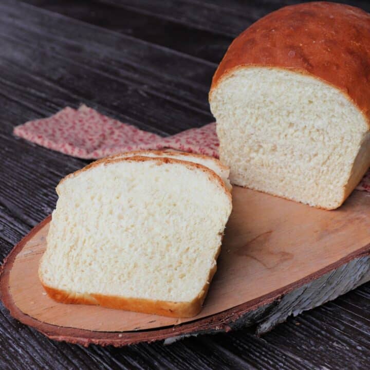 Slices of white bread sitting on a board with the remaining loaf sitting on a pink cloth behind them.