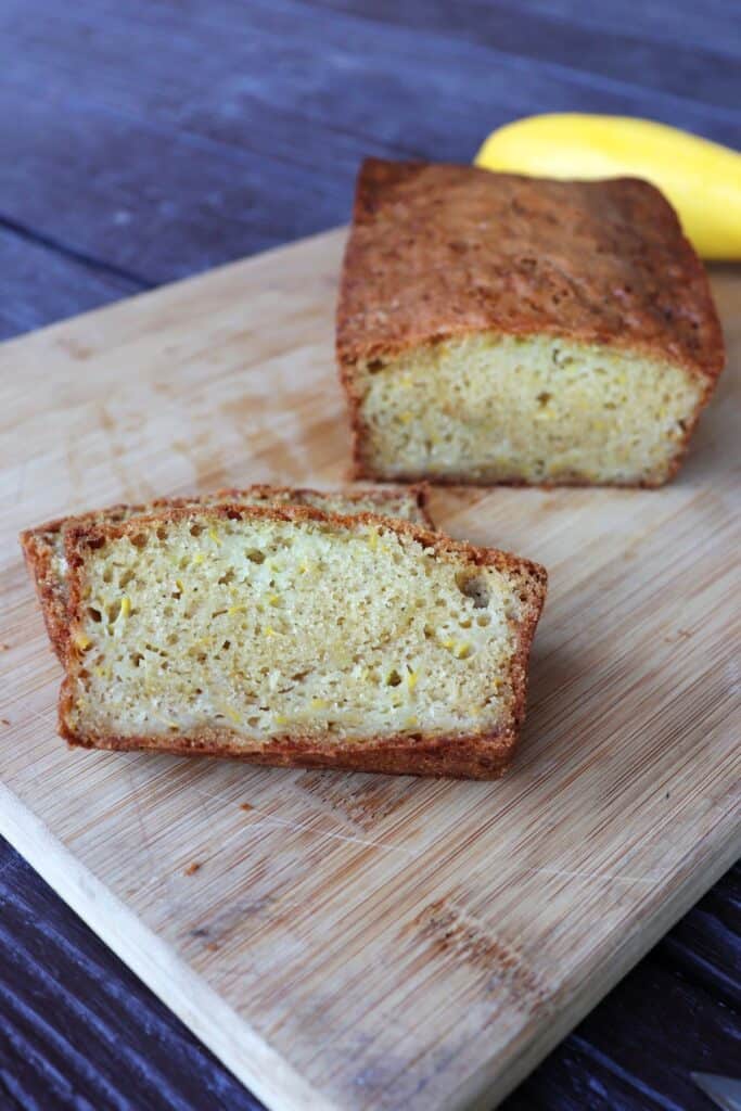 Slices of squash bread sitting on a board with remaining loaf behind it and a yellow summer squash.