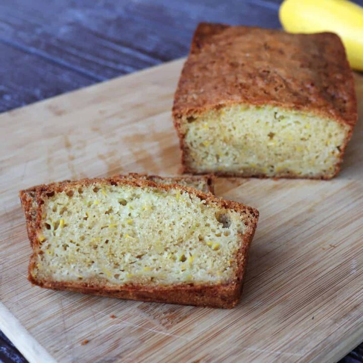 Slices of squash bread sitting on a board with remaining loaf behind it and a yellow summer squash.