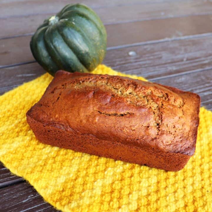 A loaf of bread sits on a yellow cloth with a whole acorn squash behind it.