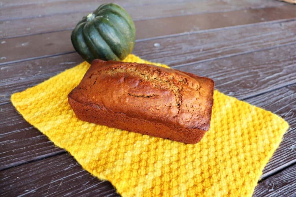 A loaf of bread sits on a yellow cloth with a whole acorn squash in the background.