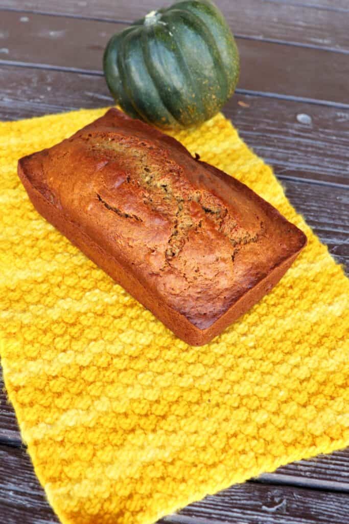 A loaf of bread sits on a yellow cloth as seen from above. A whole acorn squash sits behind the bread.