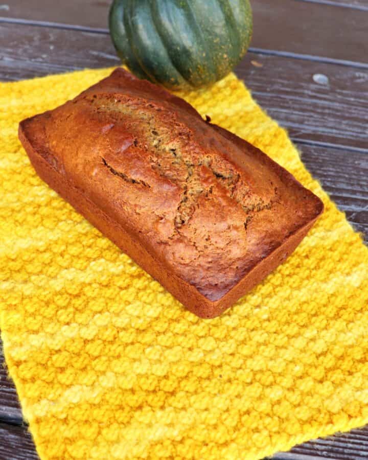 A loaf of bread sits on a yellow cloth with a whole acorn squash behind it.