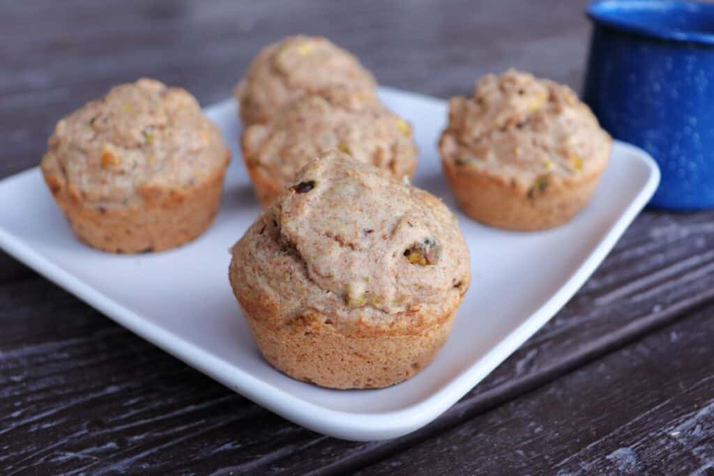 Spelt muffins sitting on a white square platter. A blue tin coffee mug in the background. 