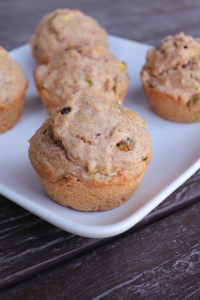 Close-up of a spelt muffin showing bits of nuts on a white platter with more muffins behind it.