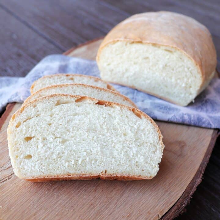 Slices of white hearth bread sit in front of the remaining loaf that is draped over a napkin on a board.