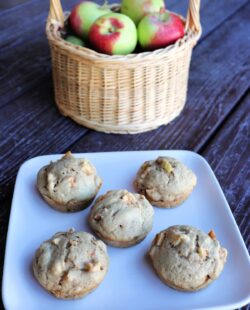 Apple spice muffins on a plate, a basket of fresh apples sits in the background.