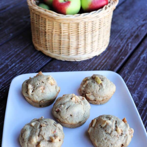 Apple spice muffins on a plate, a basket of fresh apples sits in the background.