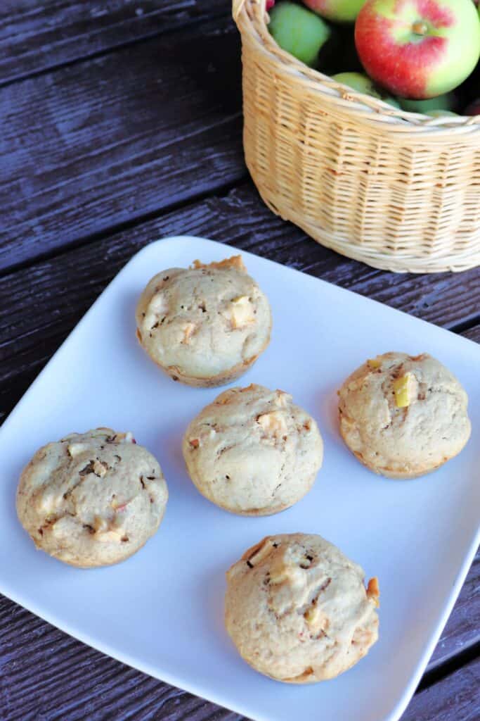 5 Apple Spice Muffins on a plate as seen from above, a basket of fresh apples sits behind it.