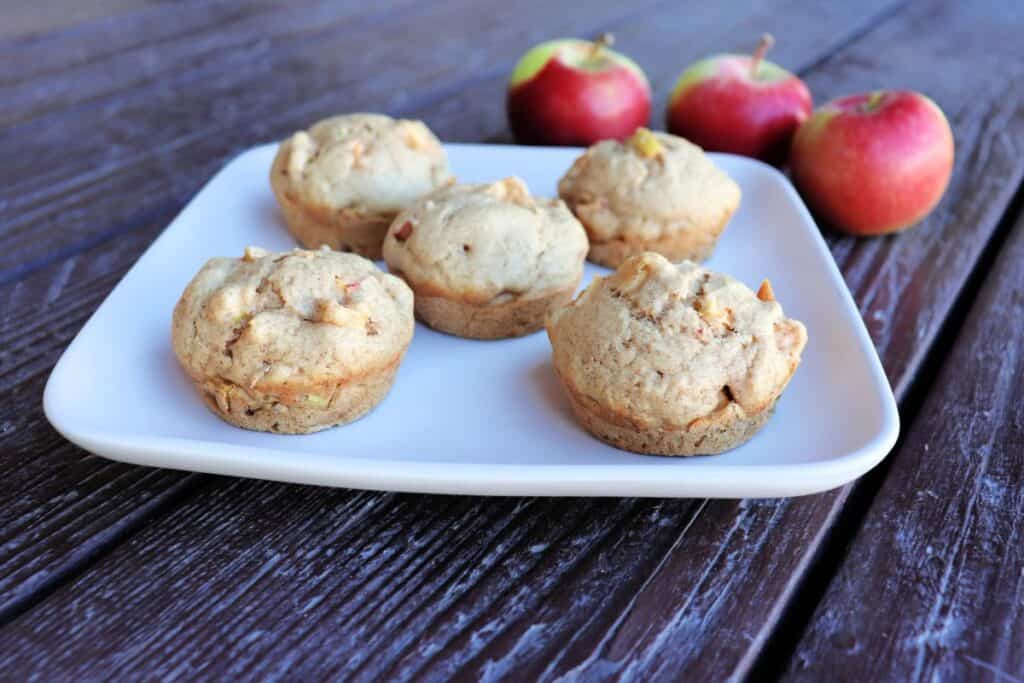 A plate of apple spice muffins with fresh apples sittng behind it.