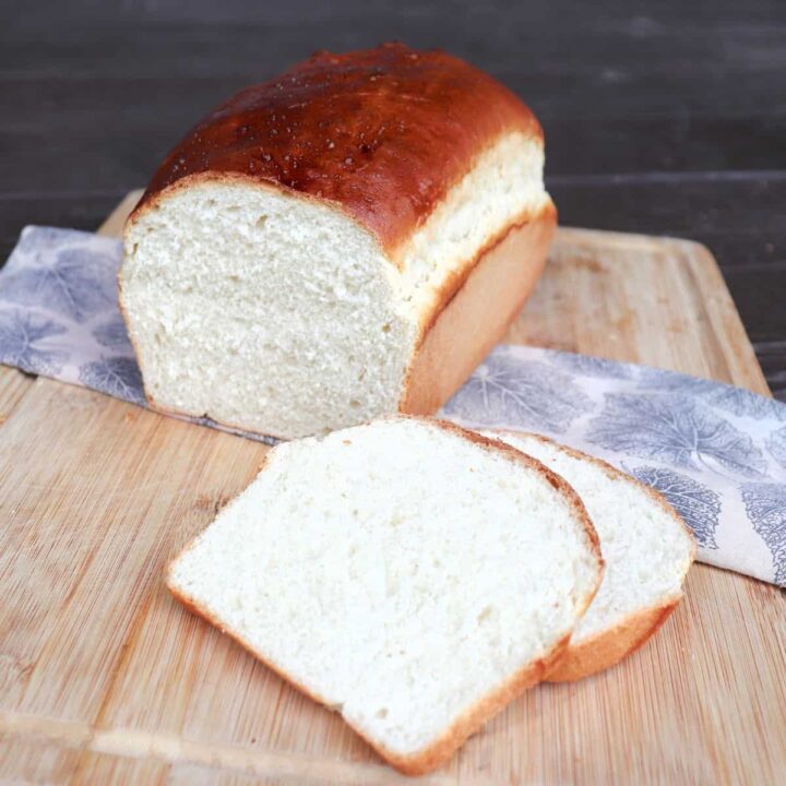 Slices of white bread sit on a board with remaining loaf siting on a cloth behind them.