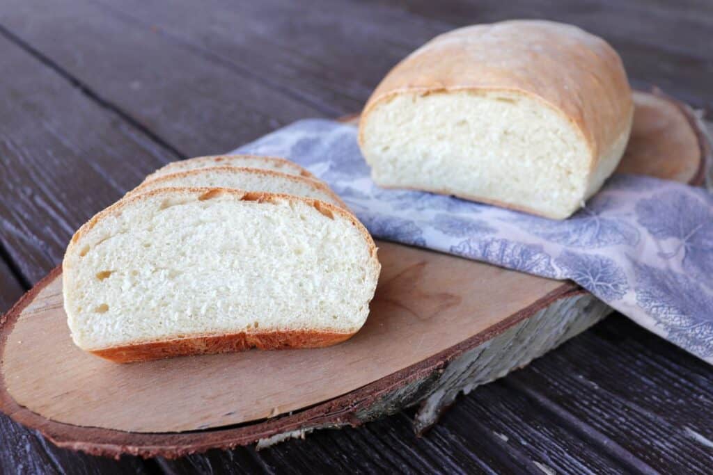 Slices of white bread sit on a board with the remaining loaf sitting on a napkin next to them.