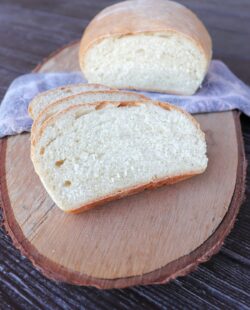 Slices of white hearth bread sit in front of the remaining loaf that is draped over a napkin on a board.