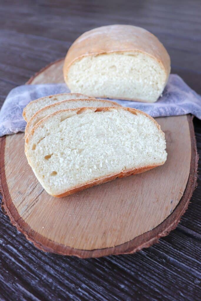 Slices of white hearth bread sit on a board, the remaining loaf sits on a napkin behind them. 