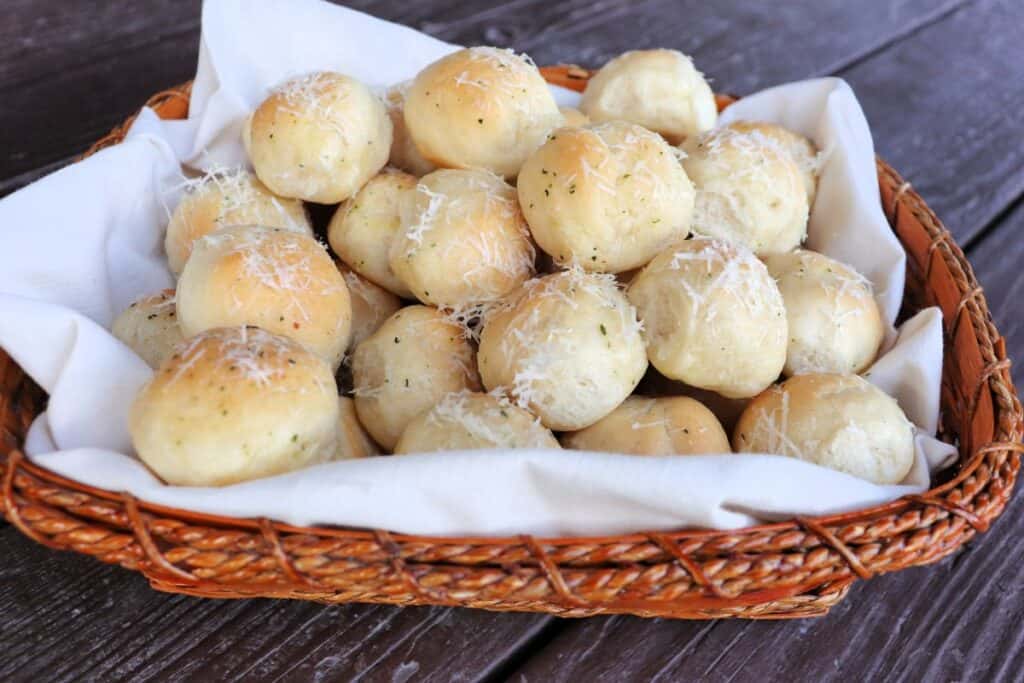 A linen lined basket full of bread balls covered in grated parmesan cheese.