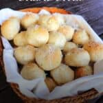 A linen lined basket full of bread balls covered in grated parmesan cheese. Text overlay reads parmesan bread bites.