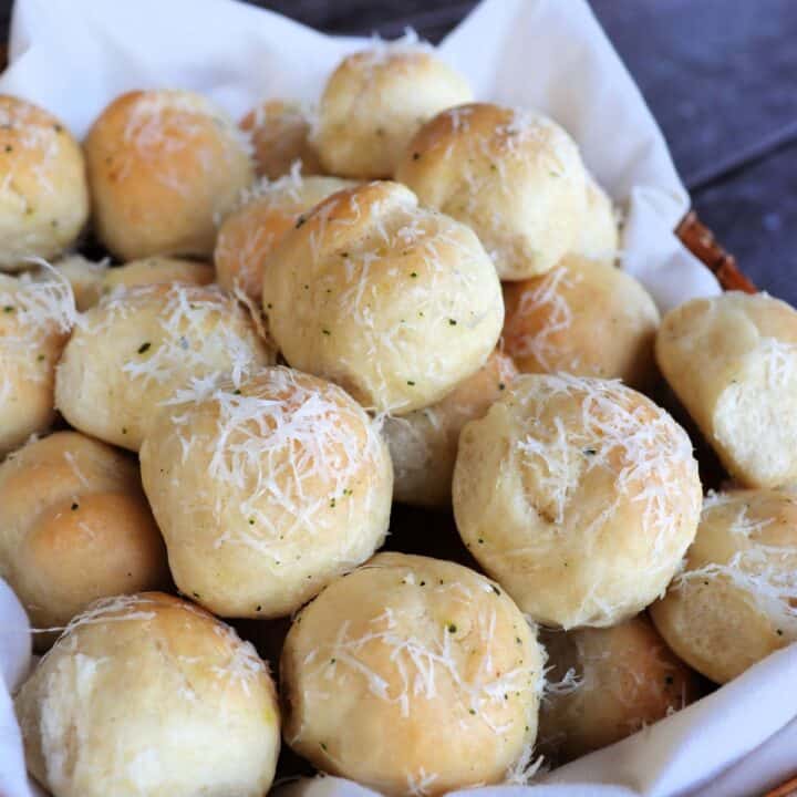 A linen lined basket full of bread balls covered in grated parmesan cheese.