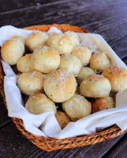 A linen lined basket full of bread balls covered in grated parmesan cheese.