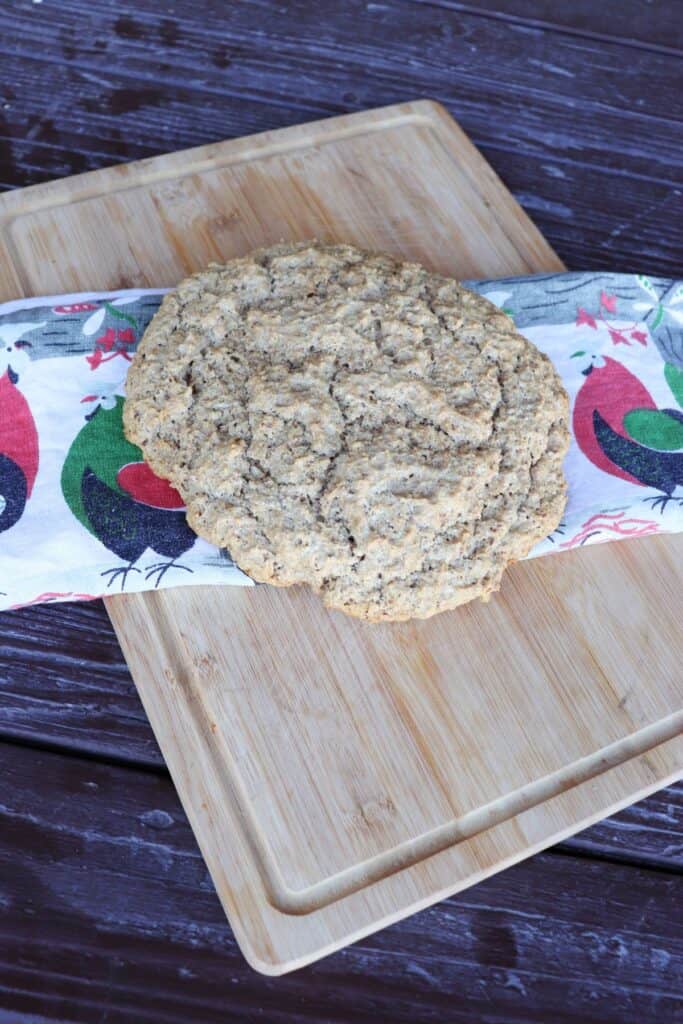 A round, flat loaf of finnish rye bread sits on top of a colorful cloth on a board.