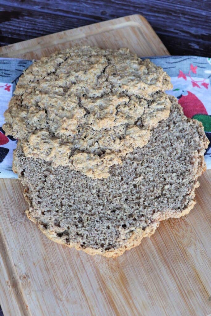 A round, flat loaf of finnish rye bread is sliced in half and sits on top of a colorful cloth on a board.