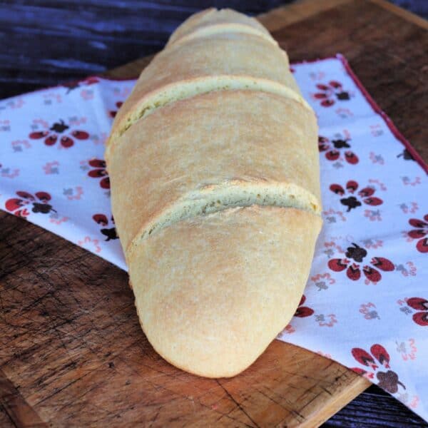 An oblong loaf of semolina bread sits on top of a printed cloth on a board.