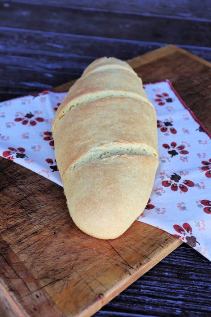 An oblong loaf of semolina bread sits on top of a printed cloth on a board.