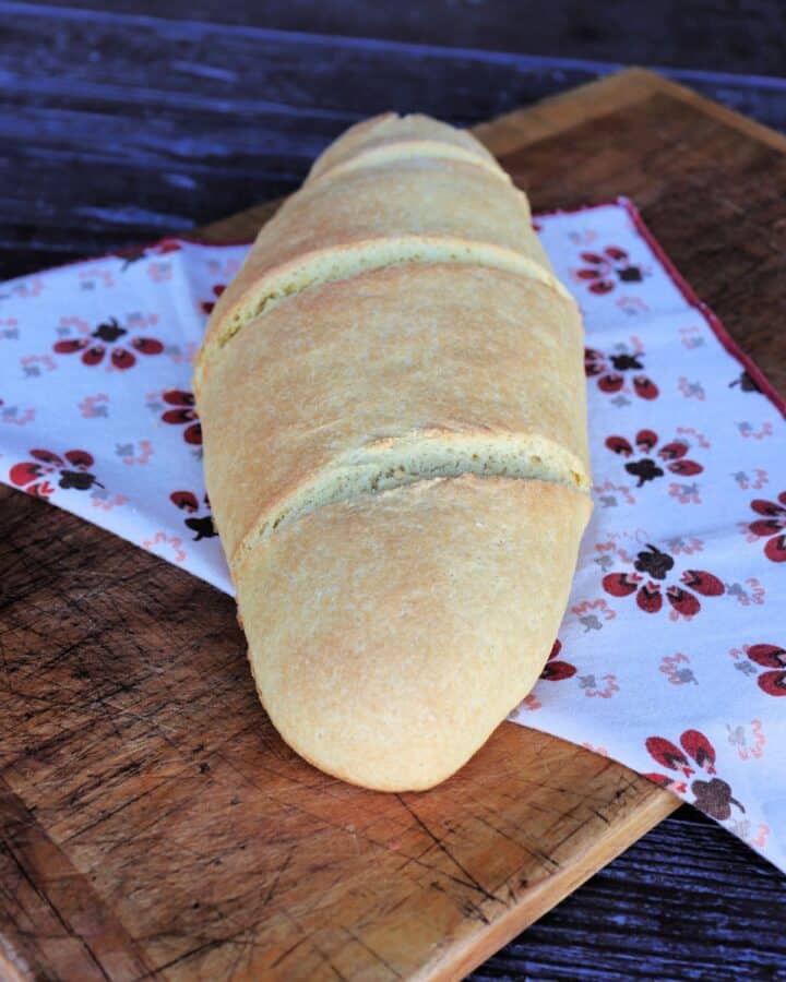 An oblong loaf of semolina bread sits on top of a printed cloth on a board.