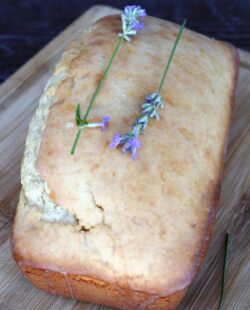 A loaf of glazed lavender with fresh lavender stems sits on a board.