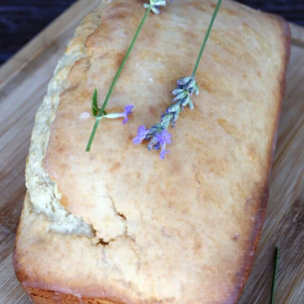 A loaf of glazed lavender with fresh lavender stems sits on a board.