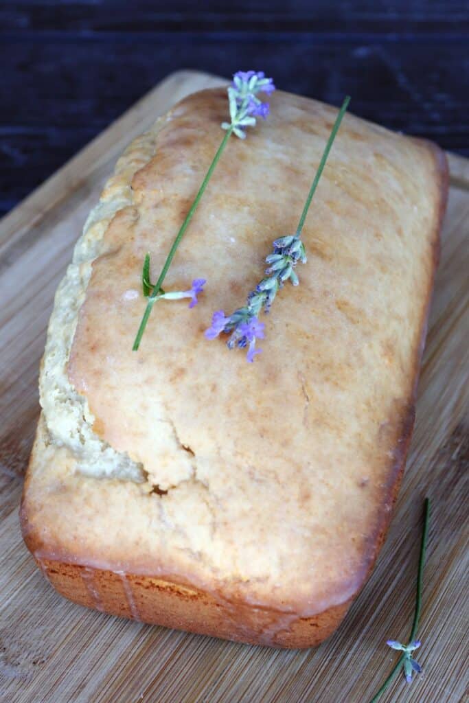 A loaf of glazed lavender with fresh lavender stems sits on a board.